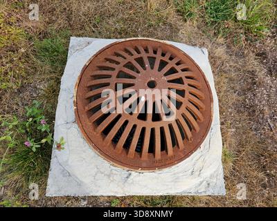 Rusty domed metal manhole grate cover storm water drain in ground Stock Photo