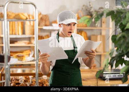 Young baker looking confused while reviewing order documents Stock Photo