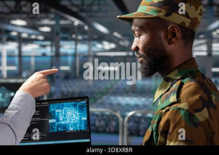 Black military IT expert in server hub using AI tools to oversee battlefield surveillance to develop warfare tactics. Army data center admin doing transmission analysis and live monitoring. Stock Photo