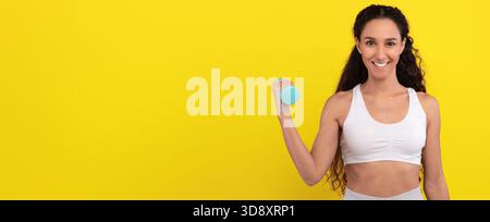 Woman Exercising With Dumbbell Against Bright Yellow Background During Fitness Routine Stock Photo