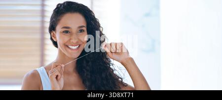 Smiling Woman Flossing Teeth While Standing in Bright Bathroom Stock Photo
