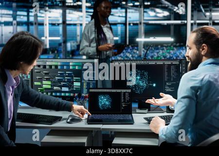 Programmers doing brainstorming in data center, using AI LLM assistant to do maintenance on equipment rigs. Server hub admins working together, using large language model chatbot to do backups Stock Photo