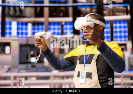 Photovoltaic engineer applies virtual reality tools to create and optimize design models for solar panel manufacturing and efficiency. African american man immersed in AR industry 4.0 training. Stock Photo
