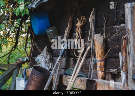 Various garden tools and farm equipment hang on the wooden wall of an old shed, reflecting rustic lifestyle, manual labor, and rural simplicity. Stock Photo