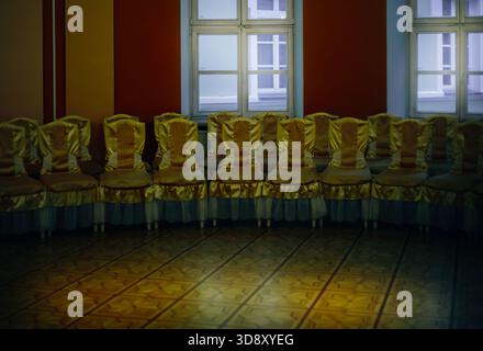 Rows of identical yellow chairs stand in a spacious hall near bright windows, creating an atmosphere of silence, readiness, and anticipation of an eve Stock Photo