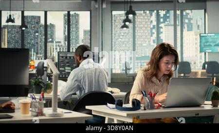 Business people using laptops and computers in bright workspace, analyzing projections, metrics and reports. Team focuses on business intel, insights and targets under executive management. Stock Photo