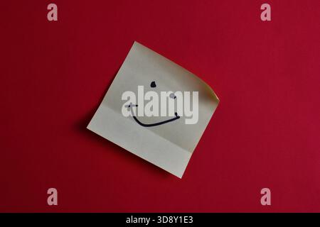 Yellow sticky note with smiley face on red background, conveying happiness and simplicity through bold color contrast and minimal design. Stock Photo