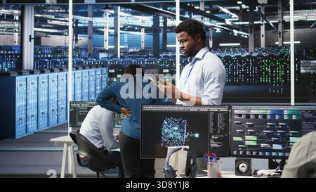 Data center technician using tablet to do node tree programming, optimizing resource allocation. Server room IT expert using predictive AI visualization systems for maintenance planning, camera A Stock Photo