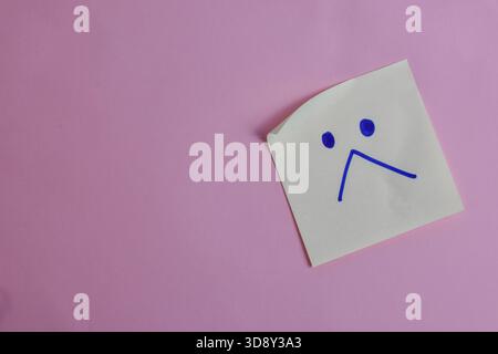 Light blue sticky note with sad face on pink background, expressing emotion through minimal design and strong visual contrast. Stock Photo