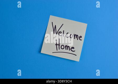 Yellow sticky note with Welcome Home message on blue background, conveying warmth and greeting through simple text and strong color contrast. Stock Photo