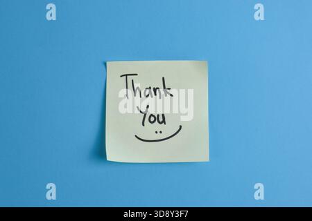 Yellow sticky note with Thank You message on blue background, conveying warmth and greeting through simple text and strong color contrast. Stock Photo