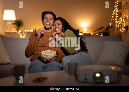 Couple Enjoys a Comedy Film Together With Popcorn Using a Home Cinema Projector Indoors Stock Photo