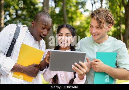 Students Enjoying Time Together in the Park While Watching Something Interesting on a Tablet During a Sunny Day Stock Photo
