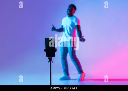 Young Man Dancing in Front of Smartphone on Tripod With Colorful Background Stock Photo