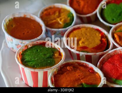 A close-up of several colorful, multi-layered steamed cupcakes in paper liners, displaying vibrant green, red, and orange tones. Stock Photo