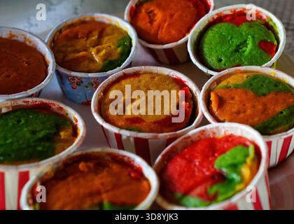 A close-up of several colorful, multi-layered steamed cupcakes in paper liners, displaying vibrant green, red, and orange tones. Stock Photo