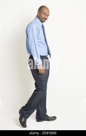 Side view Indian businessman walking and turn back head looking at camera, on plain background Stock Photo