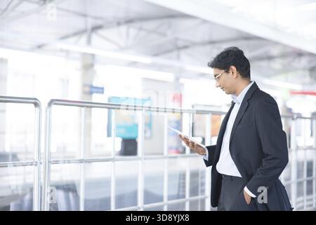 Asian Indian businessman using tablet pc while waiting train at railway station Stock Photo