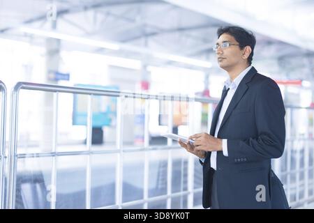 Asian Indian businessman using tablet computer while waiting train at railway station Stock Photo