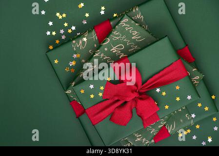 Stack of green gift boxes with red ribbon and golden and silver  star-shaped confetti  on green background Stock Photo