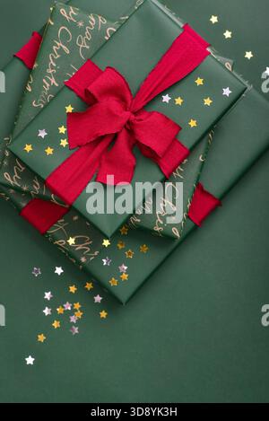 Stack of green gift boxes with red ribbon and golden and silver  star-shaped confetti  on green background Stock Photo