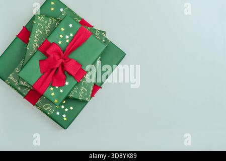 Stack of green gift boxes with red ribbon and golden and silver  star-shaped confetti  on blue background, top view Stock Photo