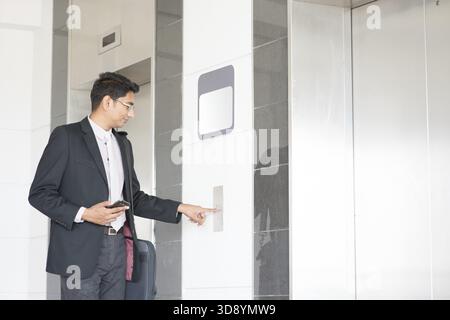 Young Indian businessman pressing on elevator button, waiting door open to enter inside the lift Stock Photo