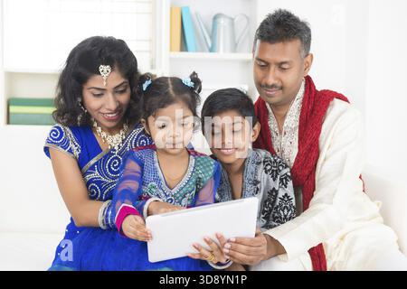 Indian Asian family using tablet pc computer at home. India family living lifestyle in traditional dress. Happy smiling parents and children Stock Photo
