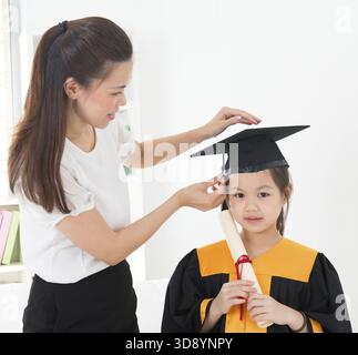Asian child graduation, teacher adjusting cap for student indoor Stock Photo
