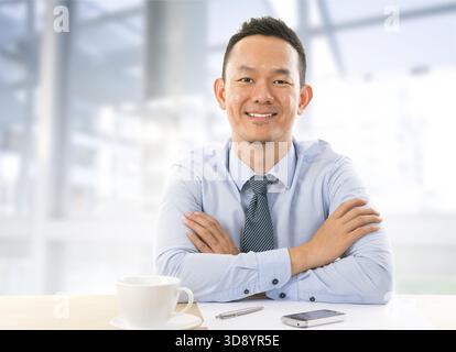 Mid aged Asian Businessman sitting at table in office Stock Photo