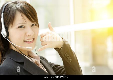 Portrait of a young Asian customer support with headset smiling, at an office environment, natural golden sunlight at background Stock Photo