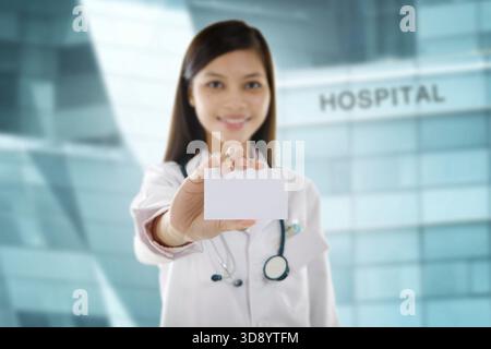 Asian Mixed-race female doctor holding business card in front hospital building Stock Photo