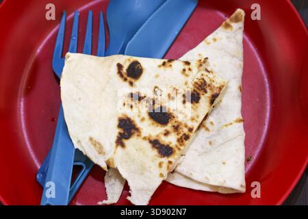 Simple meal of toasted flatbread on red plastic plate with blue cutlery. quick and easy snack or light lunch, this food represents convenient and casu Stock Photo