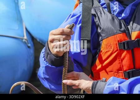 A rafting guide holding safety rope beside rushing river rapid, with ...