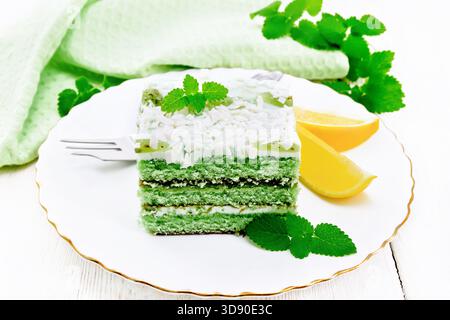Piece of cake with mint and orange, white cream, confit, green sponge cake, sprinkled with white chocolate and green jelly in a plate, towel on white Stock Photo