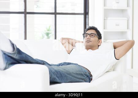 Indian guy resting and daydreaming at home. Asian man relaxed and lying on sofa indoor. Handsome male model Stock Photo