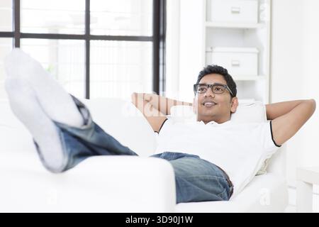 Indian guy daydreaming and rest at home. Asian man relaxed and lying on sofa indoor. Handsome male model Stock Photo