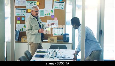 Businessmen, documents and meeting with pinboard for analytics or performance review in office. Men, employees or creative team with paperwork on Stock Photo