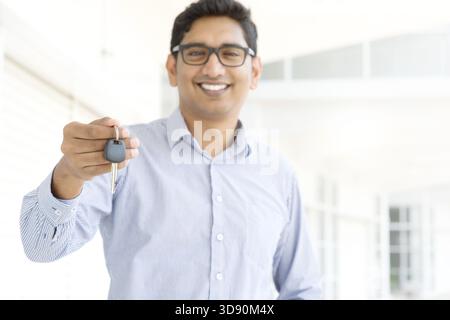 Young Asian Indian estate agent or salesman showing a key, India male business man, real modern office building as background Stock Photo
