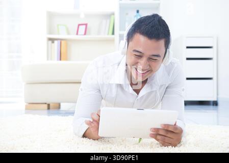 Asian man listen mp3 with headphone, lying on floor at home Stock Photo