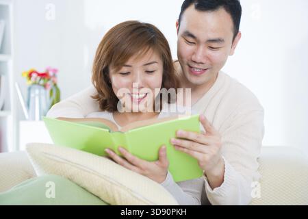 Beautiful loving Asian couple reading a book on the sofa Stock Photo