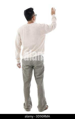 Rear view of Asian man hand touching on transparent virtual screen, space for text/button, full length standing isolated on white background Stock Photo