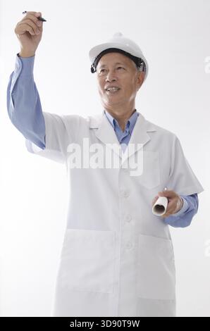 Portrait of Asian engineer with hard hat and blueprint, hand writing on blank space, standing isolated on white background Stock Photo