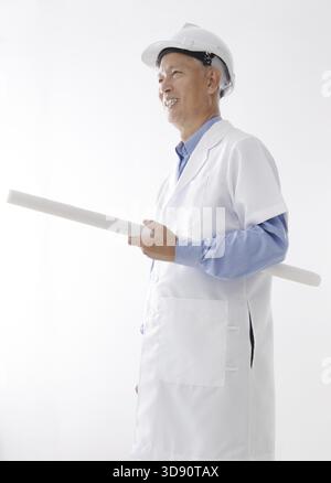 Portrait of Asian engineer with hard hat and blueprint smiling, standing isolated on white background Stock Photo