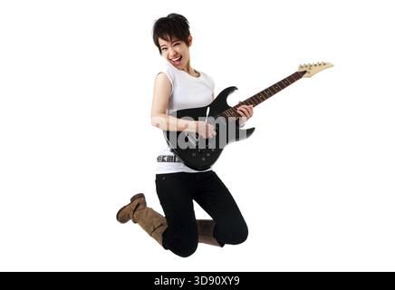 Asian female rockstar holding guitar jumping in air Stock Photo