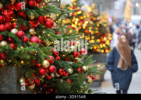 New Year decorations in winter city, Christmas trees with golden lights and toy balls on a street on blurred background of people Stock Photo