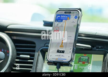A cell phone is mounted on a dashboard of a car. The phone is displaying a map and the car is on a road Stock Photo