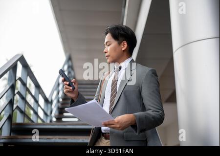 Businessman or office worker holding documents and making a phone call on flyover or overpass stairs. Go to or Get off Work, High metal footbridge. Stock Photo