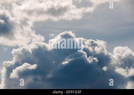 A breathtaking view of a towering, multi-layered cumulus cloud structure dominating the frame. The lower section is dark and ominous, while the sunlit Stock Photo