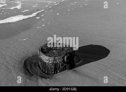 Black and white minimalist image of a weathered timber post with metal top on sand Stock Photo